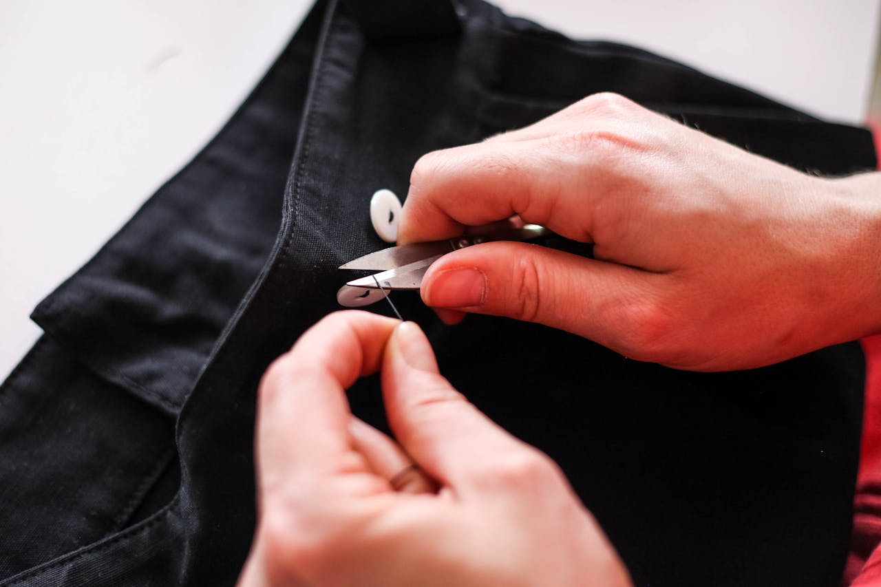 about-01 Close-up view of hands sewing black fabric with scissors, showcasing precision stitching.